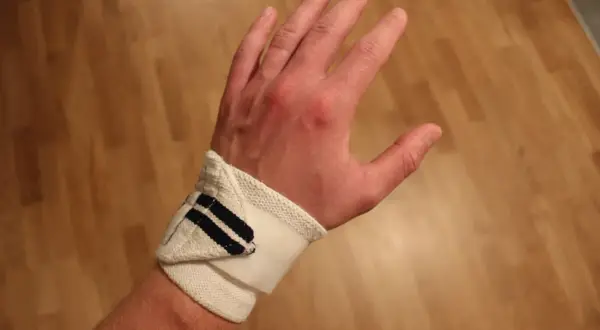 En hand med handledsskydd, kanske för att stödja en svag handled. Skyddet är vitt med mörkblå ränder.
