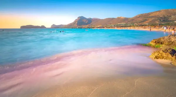 Piękna plaża w Grecji, gdzie pogoda w lutym pozwala na kąpiel w turkusowym morzu. W tle góry i kurort.