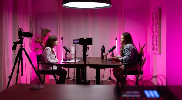 Two women are recording a podcast with a professional podcast lighting setup, featuring pink ambient light and studio microphones.