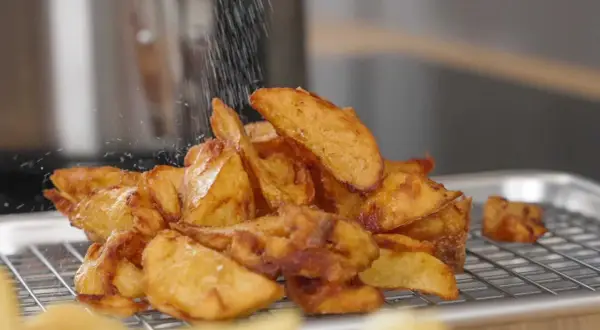 Krispiga potatisklyftor strös med salt efter frityr. Perfekt frityr temp för gyllene, läckra pommes.