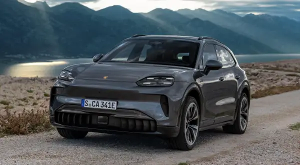 Szary Porsche Cayenne 2025 na kamienistej drodze z widokiem na góry i jezioro.