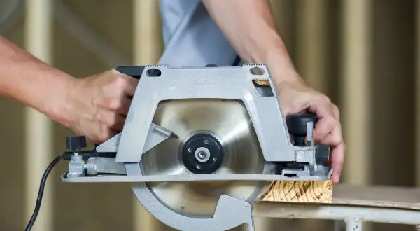 Mains d'un bricoleur utilisant une scie pour parquet stratifié, coupant une planche de bois.