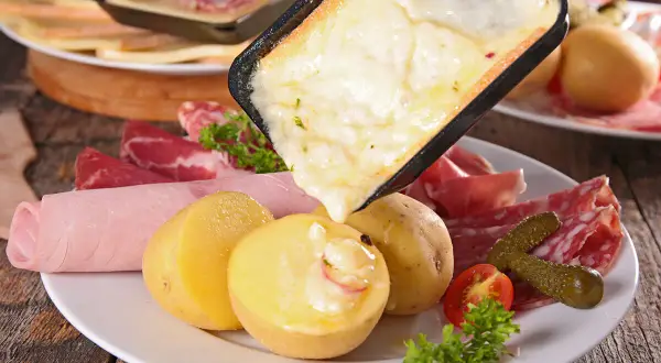 Raclette queso fundido cayendo sobre patatas, embutidos y pepinillos. ¡Una delicia para compartir!