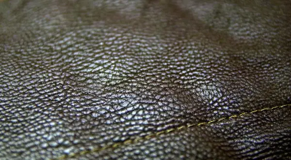 Zbliżenie na fakturę ciemnobrązowej skóry. Real leather to naturalny, trwały materiał, który pięknie się starzeje. Widoczny delikatny szew.