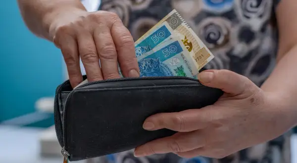 Dłonie chowają banknoty 50 zł do czarnego portfela. To może być początek oszczędzania na emeryturę, jak w funduszu Amundi Stars Silver Age.