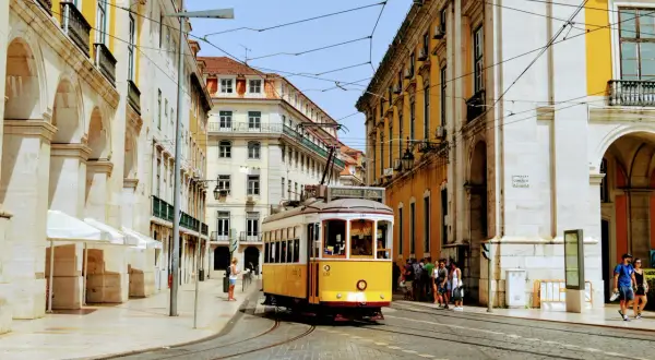 Gul lissabon spårvagn på kullerstensgata, omgiven av gul och vit arkitektur.