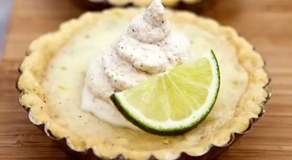 En liten citron key pie med en klick grädde och en limeklyfta.