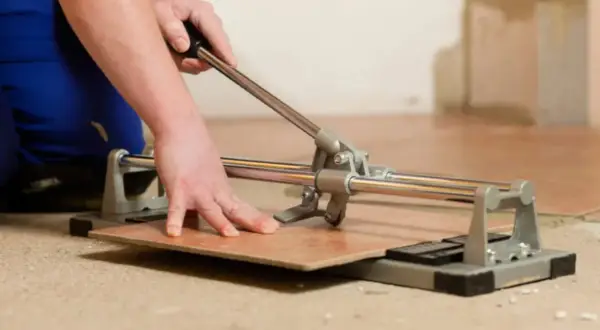 Mano che usa un tagliapiastrelle per tagliare una piastrella. Impara come forare le piastrelle con questo strumento.
