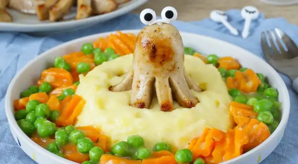 Ein lustiges gesundes Abendessen für Kinder: Würstchen-Oktopus auf Kartoffelbrei mit Erbsen und Karotten.