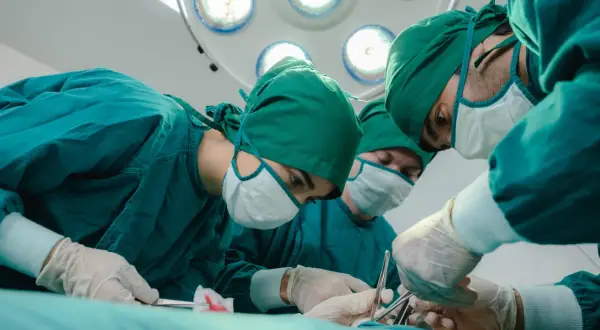 Zespół chirurgów w zielonych fartuchach i maseczkach przeprowadza operację zastawki serca. Skupienie na twarzach, precyzja ruchów.
