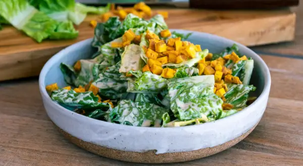 En skål med krispig romansallad, rikligt täckt med krämig caesarsallad dressing och toppad med gyllene krutonger.