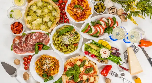 Obfity tradycyjny włoski obiad: pizze, makarony, sałatka caprese, wędliny, warzywa i ser.