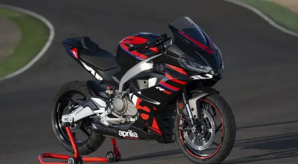 Czarny motocykl sportowy Aprilia na czerwonym stojaku na torze wyścigowym.