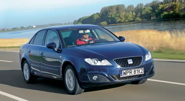 Ciemnoniebieski Seat Exeo 2.0 TDI jedzie drogą nad rzeką, kierowca w czerwonej kurtce.