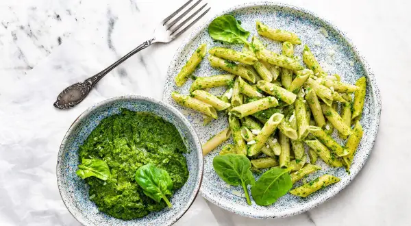 Penne z domowym pesto ze szpinaku, podane w miseczce i na talerzu, z widelcem obok.