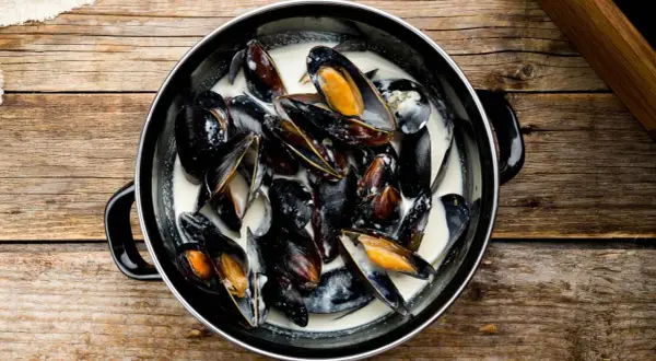 Un plat de moules à la crème, prêtes à être dégustées sur une table en bois rustique.