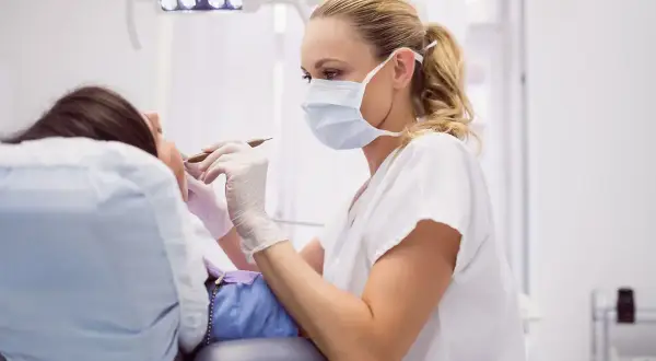 Dentystka w masce i rękawiczkach wykonuje zabieg, kiedy leczenie kanałowe jest konieczne.