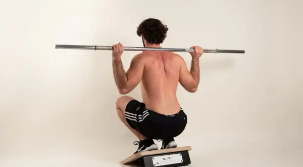 Mann mit lockigem Haar macht eine Kniebeuge mit Langhantel auf einem Trainingsgerät.