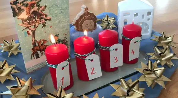Vier rote Kerzen mit Zahlen 1-4, ein Adventskalender, ein Krippenspiel und goldene Sterne schmücken den Tisch. Perfekt für die Vorfreude auf Weihnachten in der **Advent Grundschule**.