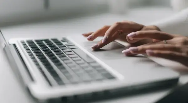 Dłonie z paznokciami malowanymi na jasny róż korzystają z touchpada laptopa.