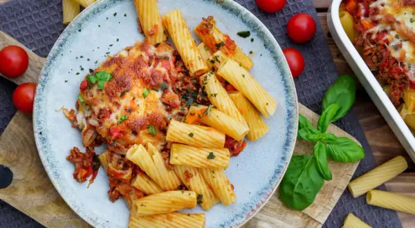 Herzhafter nudelauflauf mit hackfleisch, überbacken mit Käse, serviert mit Rigatoni und frischen Tomaten.