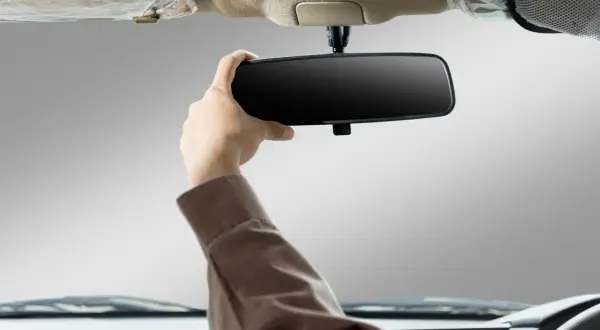 Main d'un conducteur ajustant le rétroviseur intérieur de sa voiture. Apprenez comment emboîter un rétroviseur intérieur pour une meilleure visibilité.