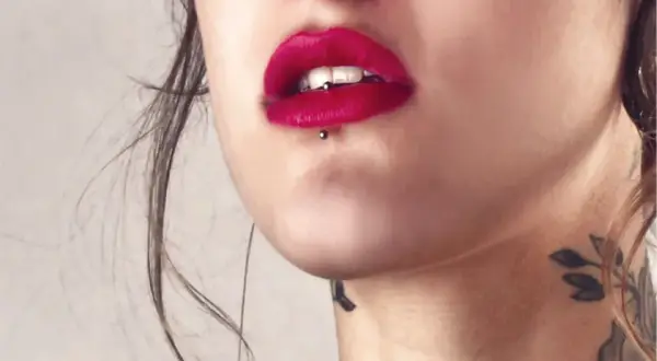 Usta z czerwoną szminką i ashley piercing. Delikatny tatuaż na szyi dodaje uroku.