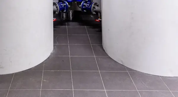 Szare płytki w kotłowni, między białymi zbiornikami. W tle widać instalację hydrauliczną z niebieskimi zaworami.