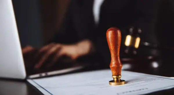Pieczęć urzędowa na dokumencie, obok laptopa i młotka sędziowskiego. Rozważane są akcje pracownicze PKP po śmierci.