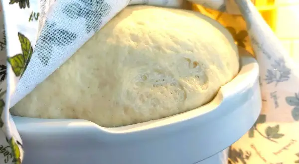 Puszyste ciasto drożdżowe rośnie pod lnianą ściereczką. Idealny czas, ile powinno rosnąć ciasto drożdżowe, to moment, gdy podwoi objętość.
