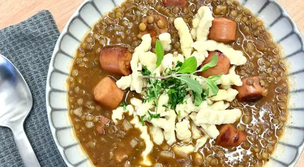 Herzhafte Linsen mit würzigen "Spotzen" (Spätzle) und Fleischwurststücken, garniert mit frischen Kräutern.