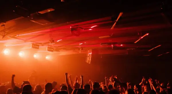 Folla in delirio in una delle tante discoteche techno, con luci laser rosse che illuminano la scena.