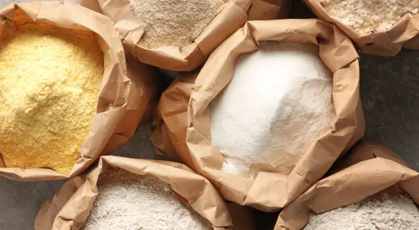Różne rodzaje mąk w papierowych torbach. Zastanawiasz się, ile glutenu ma mąka pszenna? Tutaj znajdziesz odpowiedź.