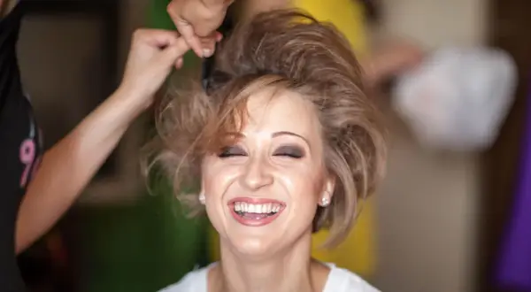 Lachende Frau, der die Haare toupiert werden für einen voluminösen Look.