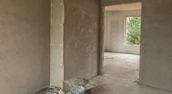 Świeżo położony tynk cementowo-wapienny na ścianach i słupie. Widać wiadro z zaprawą i kielnię. Czekamy, aż tynk wyschnie.