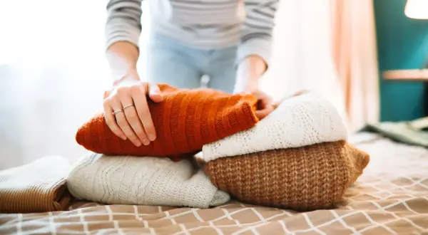 Hände falten warme Pullover. Der Wollprogramm-Waschgang ist abgeschlossen, die Kleidung ist bereit für den Schrank.