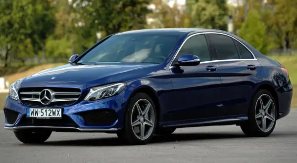 Granatowy Mercedes Klasy C, idealny do poznania jego **mercedes c klasa dane techniczne**. Elegancki sedan na tle zieleni.