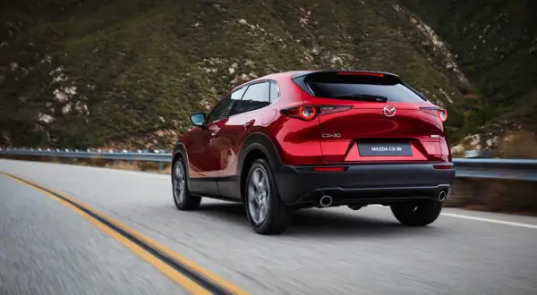 Röd Mazda CX-30 hybrid på en slingrig väg i bergen. Testkörning av den nya modellen.