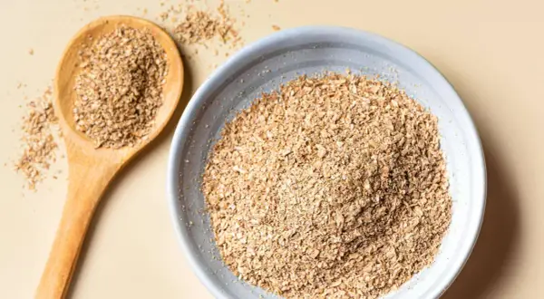 Eine Holzschale und ein Löffel gefüllt mit Haferkleie. Haferkleie ist ein nährstoffreiches Nebenprodukt der Haferverarbeitung.