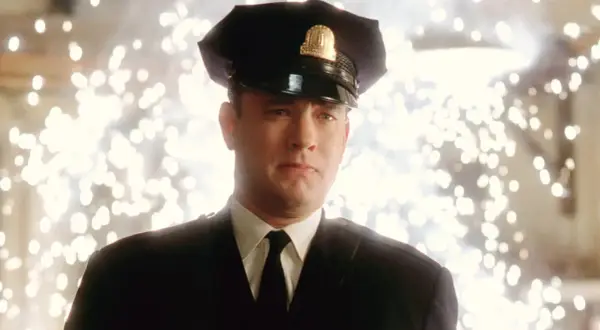 Tom Hanks w mundurze strażnika w jednym z jego filmów. Tło rozświetlone jest fajerwerkami.