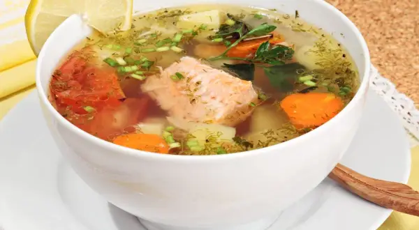 Aromatic rosyjska zupa rybna z łososiem, ziemniakami, marchewką i pomidorami, ozdobiona cytryną i koperkiem.