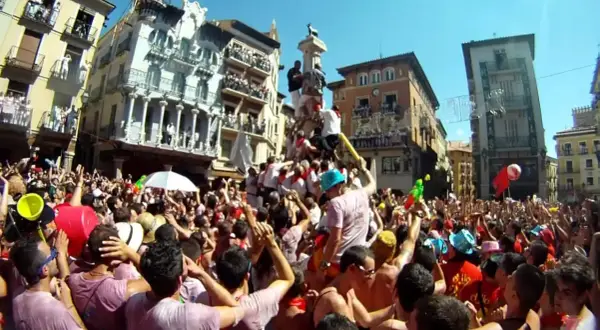 Multitud celebra cuando son vaquillas en Teruel. Gente en una plaza con edificios históricos, algunos subidos a un monumento.