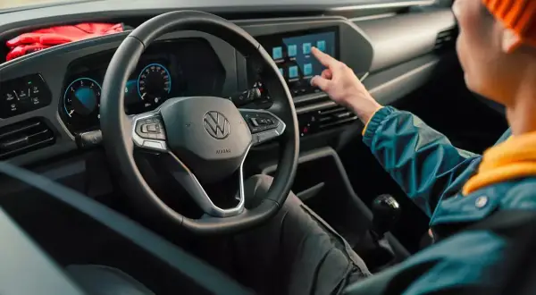 Interni moderni del Volkswagen Caddy: un utente interagisce con il touchscreen centrale, mentre il volante e il cruscotto digitale sono ben visibili.