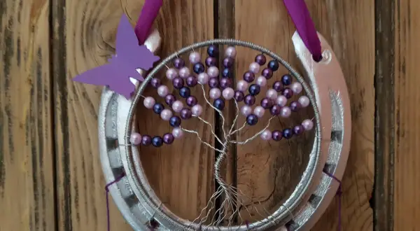 Tuto attrape rêve arbre de vie : un fer à cheval argenté orné d'un arbre de vie en fil de fer et perles violettes et roses, avec un papillon violet.