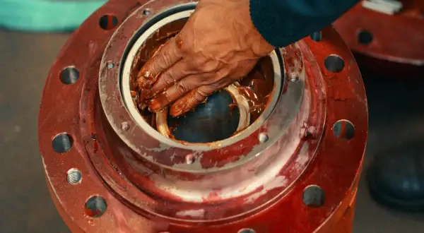 Ręka smaruje łożysko brązowym smarem. To smar silikonowy do czego? Do ochrony i smarowania elementów mechanicznych.