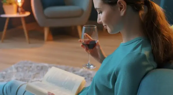 Kobieta z kieliszkiem wina czyta książki. Może to być jedna z fascynujących powieści Joanny Jax, która wciąga w swój świat.