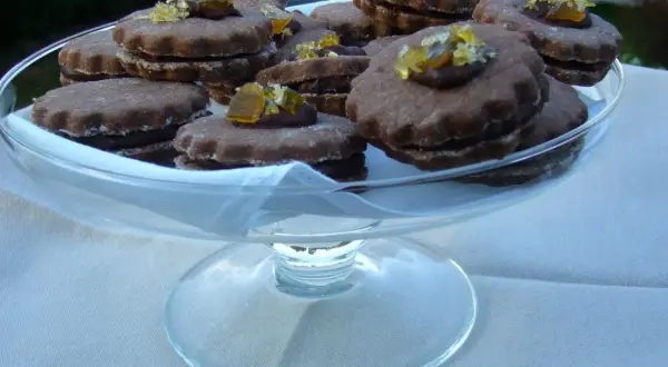 Gourmandes bouchées de biscuits fourrés chocolat, ornées de zestes d'agrumes confits, présentées dans une coupe en verre.