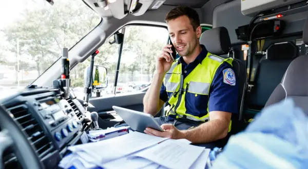 Paramédic en uniforme, parlant au téléphone et consultant une tablette dans un véhicule prioritaire, respectant le code de la route.