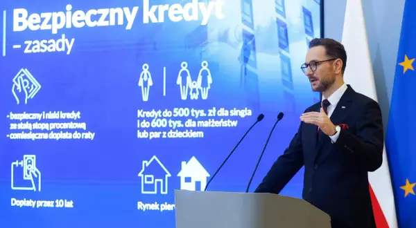 Mężczyzna w garniturze prezentuje zasady "Bezpiecznego kredytu" z dopłatą do rat. Program oferuje kredyt 2 procent dla singli i małżeństw.