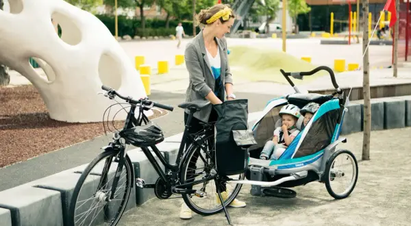 Frau mit Fahrrad und Kinderanhänger, bereit für eine Ausfahrt. Sie genießt das Fahrrad fahren, auch in der Schwangerschaft.